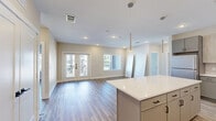 Located in Spring, Texas, this well-appointed single-story home offers three bedrooms, two bathrooms, and three closets within a thoughtfully designed floor plan. Light-toned luxury vinyl plank flooring flows consistently throughout the living areas and bedrooms, complementing the neutral warm-beige color palette that creates a bright, cohesive ambiance.

The open-concept kitchen is a standout feature, showcasing two-tone cabinetry with light wood upper cabinets and gray lower cabinets, a vertical subway tile backsplash, white quartz countertops, stainless steel appliances, and a large central island with pendant lighting above. The kitchen connects seamlessly to the living area, which features recessed lighting and French doors that invite natural light.

The primary bedroom is generously sized with a ceiling fan, and its ensuite bathroom includes marble-look porcelain tile flooring, a glass-enclosed walk-in shower with matte black fixtures, and direct access to a walk-in closet with built-in shelving and double hanging rods. The secondary bathroom features the same marble-look tile and a soaking tub with a shower combo. Additional bedrooms are bright and airy, benefiting from multiple windows with outdoor views.