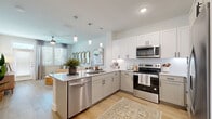 Located in Wesley Chapel, FL, this well-designed one-bedroom, one-bathroom residence offers a thoughtful layout that maximizes every square foot. The open-concept kitchen and living area forms the heart of the home, where light wood-tone flooring, soft neutral walls, and large windows allow natural light to flow freely throughout. The kitchen is outfitted with crisp white and grey shaker-style cabinetry, a white subway tile backsplash, stone countertops, a peninsula with a built-in sink and dishwasher, and a full suite of stainless steel appliances. Pendant lighting above the peninsula adds a refined touch. The living area is bright and welcoming, featuring a ceiling fan, a glass-paned door leading to the outdoors, and ample room for comfortable furnishings. The bedroom offers plush carpeting, a ceiling fan, and large windows dressed with elegant drapes that invite soft, diffused light. The bathroom is finished with grey shaker-style cabinetry, stone countertops, a large vanity mirror, and light wood flooring, with direct access to a dedicated walk-in closet complete with built-in shelving and hanging rods. The overall ambiance is clean, modern, and inviting throughout.