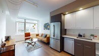 This thoughtfully designed single-floor residence offers a seamless blend of modern aesthetics and functional living. The open-concept layout connects the kitchen and living area, creating an inviting and efficient use of space. The kitchen is outfitted with stainless steel appliances — including a French door refrigerator, gas range with over-the-range microwave, and dishwasher — complemented by two-tone cabinetry featuring white upper cabinets and dark lower cabinets, along with light quartz countertops. An architectural highlight is the prominent exposed ductwork that runs along the ceiling, lending an industrial-modern character to the interior.

The living area is anchored by large floor-to-ceiling windows that flood the space with natural light and offer views of the surrounding urban landscape. Warm hardwood-style flooring runs throughout, creating a cohesive flow between rooms.

A hallway connects the living spaces to the bedroom, which features a closet, a large window, and a calm, neutral palette. The full bathroom is finished with wood-look tile flooring, a streamlined vanity with under-mount sink, and a clean, bright layout. The overall ambiance is contemporary and polished, combining urban sophistication with comfortable, practical design.
