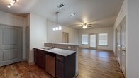 This single-floor residence offers a thoughtfully designed open-concept layout that seamlessly connects the kitchen, dining, and living areas. The kitchen serves as a central hub, featuring dark espresso cabinetry, granite countertops with a tile backsplash, stainless steel appliances including a dishwasher and refrigerator, and a peninsula with a double sink that overlooks the main living space. Pendant lighting above the peninsula and a ceiling fan in the living area add functional style. Natural light filters in through blinds-fitted windows, and a set of French doors at the rear of the living area provides additional brightness.

Wood-look plank flooring extends throughout the main living areas and primary bedroom, lending warmth and continuity to the space. The generously sized primary bedroom includes a ceiling fan, a window for natural light, and direct access to a private en-suite bathroom. This bathroom is appointed with granite countertops, dark cabinetry, a large mirror, and a tub-shower combination. Additional bedrooms feature plush carpeting and ceiling fans, with one offering direct access to a second full bathroom that mirrors the same granite and dark-cabinet finishes. The overall aesthetic is clean, modern, and cohesive throughout.