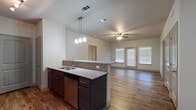 This single-floor residence offers a thoughtfully designed open-concept layout that seamlessly connects the kitchen, dining, and living areas. The kitchen serves as a central hub, featuring dark espresso cabinetry, granite countertops with a tile backsplash, stainless steel appliances including a dishwasher and refrigerator, and a peninsula with a double sink that overlooks the main living space. Pendant lighting above the peninsula and a ceiling fan in the living area add functional style. Natural light filters in through blinds-fitted windows, and a set of French doors at the rear of the living area provides additional brightness.

Wood-look plank flooring extends throughout the main living areas and primary bedroom, lending warmth and continuity to the space. The generously sized primary bedroom includes a ceiling fan, a window for natural light, and direct access to a private en-suite bathroom. This bathroom is appointed with granite countertops, dark cabinetry, a large mirror, and a tub-shower combination. Additional bedrooms feature plush carpeting and ceiling fans, with one offering direct access to a second full bathroom that mirrors the same granite and dark-cabinet finishes. The overall aesthetic is clean, modern, and cohesive throughout.