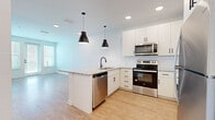 Located at 1425 14th St W in Bradenton, Florida, this well-appointed one-bedroom, one-bathroom unit offers a thoughtfully designed layout across a single floor. The open-concept kitchen and living area forms the heart of the space, showcasing crisp white shaker cabinetry with matte black hardware, a classic white subway tile backsplash, and granite countertops with a subtle speckled finish. A peninsula with pendant lighting provides additional workspace and casual seating. The kitchen is equipped with a full suite of stainless steel appliances, including a refrigerator, electric range, over-the-range microwave, and dishwasher. Light wood-style flooring flows throughout the main living areas, lending a clean, contemporary feel. The living room receives generous natural light through a set of double doors flanked by windows fitted with blinds, creating a bright and airy atmosphere. The bedroom features plush carpet flooring and dual windows that bring in additional natural light. The bathroom mirrors the home's cohesive design with a white vanity, granite countertop, matte black fixtures, a large framed mirror, and warm vanity lighting. A dedicated closet completes this efficiently designed and modern unit.