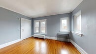 Located at 268 Alexander St in Rochester's vibrant 14607 neighborhood, this single-floor, three-bedroom, one-bathroom unit combines classic architectural character with functional living. Warm hardwood floors run throughout the entire space, complemented by crisp white crown molding and wide baseboards that frame each room with timeless detail.

The living areas are bathed in natural light through multiple white-trimmed double-hung windows, with views of the surrounding neighborhood streetscape. Cast-iron radiators in each room are a nod to the building's historic charm while providing reliable heat. The walls throughout are painted a soft, cool blue-gray, lending a calm and cohesive atmosphere.

The primary bedroom is a well-proportioned space featuring a ceiling fan and its own radiator and window, while the additional two bedrooms offer comparable finishes and natural light. Rich, dark-stained wood panel doors with brass hardware add a period-appropriate detail throughout the unit.

The kitchen is accessed through a distinctive arched entryway and features dark wood cabinetry, laminate countertops, a gas range, and a drop-panel ceiling with overhead lighting. The bathroom is highlighted by a classic clawfoot soaking tub, penny-tile flooring, a wood vanity with a wall mirror, and gray tile wainscoting — a standout vintage feature of the unit.