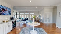 Located at 102 Carrington Rd in Hendersonville, Tennessee, this single-floor community space offers a thoughtfully designed open-plan layout that maximizes functionality and natural light. Rich hardwood flooring extends throughout, complemented by crisp white crown molding and soft gray walls that create a clean, contemporary aesthetic.

The living area is organized into distinct functional zones. A lounge area features a neutral sofa, glass coffee table, and plush navy accent chairs arranged on a textured area rug. Adjacent to this, a dining zone provides a round wooden table with tan leather chairs, positioned near floor-to-ceiling French doors with transom windows that invite abundant natural light and outdoor views.

A standout feature is the glass-partitioned fitness room, enclosed by sleek black-framed walls, housing cardio equipment and workout machines while maintaining visual openness. A beverage station with a built-in refrigerator and mounted television adds convenience near the entrance zone.

The welcoming entry features a teal accent wall, large glass storefront doors, and recessed lighting overhead. Throughout the space, recessed lighting and crown molding details reinforce a polished, well-maintained atmosphere suited for community gathering and everyday use.