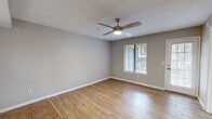 Located in Tallahassee, FL, this single-story, 2-bedroom, 1-bathroom residence offers a well-organized layout across a comfortable footprint. The living room features warm wood-look laminate flooring, neutral gray walls, a ceiling fan with light fixture, and access to an exterior door with sidelight windows that invite natural light into the space. The kitchen is equipped with stainless steel appliances including a refrigerator and electric range with a glass cooktop, white cabinetry with dark hardware, an under-cabinet range hood, and light stone countertops. Tile flooring runs throughout the kitchen, and a pass-through opening connects to adjacent living areas. Both bedrooms are carpeted and finished with neutral tones, ceiling fans, and window blinds that provide outdoor views of the surrounding tree-lined community. The primary bedroom offers a mirrored sliding closet and direct access to the shared bathroom. The bathroom includes tile flooring, a wide vanity with an integrated sink, a large wall mirror, and a separate toilet area. The multi-story residential community exterior features mature trees and covered entry areas. Overall, the space presents a clean, functional, and move-in ready environment.