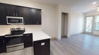 This single-floor, one-bedroom, one-bathroom residence combines modern design with functional living across a thoughtfully arranged floor plan. Light gray wood-look flooring runs throughout, lending a clean and cohesive aesthetic to every room.

The kitchen is a standout feature, showcasing rich dark cabinetry with sleek hardware that creates a striking contrast against the white quartz countertops. A full suite of stainless steel appliances — including a refrigerator, electric range, built-in microwave, and dishwasher — completes the space. A peninsula island provides additional prep space and casual seating potential, while recessed and track lighting illuminate the area effectively.

The open living area is bright and welcoming, benefiting from a sliding glass door that frames natural views of surrounding trees and allows ample natural light to fill the room. A ceiling fan adds comfort and airflow. The bedroom mirrors this approach with its own ceiling fan and a clean, versatile layout.

The bathroom features classic white subway tile surrounding a full soaking tub with shower, complemented by tile flooring and dark vanity cabinetry that echoes the kitchen's design language. The overall ambiance is modern, neutral, and move-in ready.