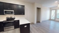 This single-floor, one-bedroom, one-bathroom residence combines modern design with functional living across a thoughtfully arranged floor plan. Light gray wood-look flooring runs throughout, lending a clean and cohesive aesthetic to every room.

The kitchen is a standout feature, showcasing rich dark cabinetry with sleek hardware that creates a striking contrast against the white quartz countertops. A full suite of stainless steel appliances — including a refrigerator, electric range, built-in microwave, and dishwasher — completes the space. A peninsula island provides additional prep space and casual seating potential, while recessed and track lighting illuminate the area effectively.

The open living area is bright and welcoming, benefiting from a sliding glass door that frames natural views of surrounding trees and allows ample natural light to fill the room. A ceiling fan adds comfort and airflow. The bedroom mirrors this approach with its own ceiling fan and a clean, versatile layout.

The bathroom features classic white subway tile surrounding a full soaking tub with shower, complemented by tile flooring and dark vanity cabinetry that echoes the kitchen's design language. The overall ambiance is modern, neutral, and move-in ready.