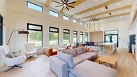 Located at 970 Upper Brook Ct in Charlottesville, VA, this single-floor space offers a thoughtfully designed open-plan layout that seamlessly integrates a living room, dining room, and kitchen into one cohesive environment. The architecture is defined by dramatically soaring ceilings accented with exposed wood beams and large ceiling fans, creating an airy, voluminous atmosphere throughout.

The living area is anchored by a built-in media wall featuring a linear fireplace, subway tile surround, and integrated shelving, with light hardwood flooring extending across the entire space. A wall of black-framed floor-to-ceiling windows floods the interior with abundant natural light and offers generous views of the lush green surroundings outside.

The dining area accommodates a large wood table with colorful modern chairs, positioned directly beside expansive windows that frame verdant outdoor views, making it a bright and inviting gathering spot. Adjacent to it, the kitchen is outfitted with white cabinetry, a light gray subway tile backsplash, stainless steel appliances, and a generous quartz-topped island with bar seating. Warm wood pendant lighting above the island adds a refined touch. A steel-framed glass entry door provides an elegant transition to the exterior, completing this bright, contemporary space.