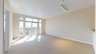 This single-floor unit is designed with a clean, functional layout that maximizes natural light and open space. The living area is generously proportioned, featuring neutral carpet, warm beige walls, and large floor-to-ceiling windows that frame panoramic outdoor views of the surrounding cityscape and distant mountains. A sliding glass door opens to a balcony, further connecting the interior to the outdoors. Track lighting on the ceiling provides flexible illumination, while a baseboard heating unit runs along the exterior wall.

The galley-style kitchen is efficiently arranged, featuring light wood cabinetry with dark countertops, wood-look flooring, and a full suite of white appliances including a dishwasher, refrigerator, range, and over-the-range microwave. A pass-through counter opens the kitchen toward the living space, enhancing the sense of connectivity.

The bedroom is carpeted and well-lit by a large window offering city and mountain views, with a baseboard heater positioned below. The full bathroom includes wood-look flooring, a single-sink vanity with dark countertop, light wood cabinetry, and a standard tub-shower combination. A dedicated laundry closet houses a stacked washer and dryer unit on wood-look flooring, adding practical convenience to the space.