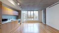 Located in the heart of Portland, Oregon, this two-floor urban residence at 1732 SW 4th Ave blends modern design with industrial character. The open-concept main living area is defined by striking exposed concrete ceilings, warm hardwood floors, and large floor-to-ceiling windows that frame expansive city views, flooding the space with abundant natural light. Track lighting complements the raw architectural aesthetic throughout.

The kitchen features sleek, warm-toned wood cabinetry paired with clean white countertops, stainless steel appliances including a built-in oven, and a tile backsplash — all seamlessly integrated into the open living space. A structural column adds an architectural detail that reinforces the industrial-modern character of the home.

The bathrooms are thoughtfully designed, with one full bath offering a tub-shower combination, mosaic tile flooring, and wood-toned cabinetry, while a second half-bath features hardwood floors and a matching vanity. Additional rooms continue the consistent design language of exposed concrete ceilings, light hardwood floors, and crisp white walls, creating versatile, light-filled spaces. The overall ambiance is clean, contemporary, and urban — ideal for those seeking a sophisticated city lifestyle in Portland's dynamic SW corridor.