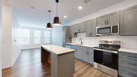 Located at 2223 Lee Rd in Cleveland Heights, Ohio, this thoughtfully designed one-bedroom, one-bathroom unit offers a modern open-concept layout that maximizes every square foot of its compact footprint. Rich hardwood-style flooring flows through the main living areas, anchoring a contemporary aesthetic defined by clean lines and neutral tones.

The kitchen is a standout feature, showcasing grey shaker-style cabinetry extending to the ceiling for generous storage, a crisp white countertop, a full suite of stainless steel appliances, and a central island with seating — all illuminated by stylish matte black pendant lights. The kitchen opens seamlessly into the living room, which is brightened by a trio of large windows that invite natural light and offer views of the surrounding neighborhood.

The bedroom features plush carpeting and a clean, airy atmosphere, complemented by a dedicated walk-in closet outfitted with built-in shelving and hanging rods for organized storage. The bathroom is finished with a dark grey vanity, white countertop, a frameless glass shower, wood-look tile flooring, and polished chrome fixtures, creating a sleek and functional space. Paneled interior doors and recessed lighting complete the unit's cohesive, contemporary feel.