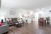 Located at 10900 Bluffside Dr in the Studio City neighborhood of Los Angeles, this single-floor unit offers a practical and comfortable layout throughout. The living room serves as the heart of the space, featuring rich hardwood-style flooring, a large sliding glass door that allows natural light to fill the room, and a wall-mounted air conditioning unit for climate control. A ceiling fan with integrated lighting adds functionality to the adjoining dining area, which comfortably accommodates a four-seat table. The open-concept design connects the living and dining areas seamlessly to the kitchen, which is separated by a half-wall peninsula. The kitchen is equipped with white cabinetry, granite-style countertops, a double-basin sink, a gas range, and a built-in microwave, providing ample storage and prep space. The bedroom is generously sized, featuring soft wall-to-wall carpeting, a large window with vertical blinds, a mirrored sliding-door closet, and a dedicated vanity area. A full bathroom with a shower-tub combination and hardwood-style flooring completes the unit. Textured ceilings are present throughout, and the clean white walls create a bright, neutral backdrop across all rooms.