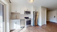 Located at 969 Hopmeadow St in Simsbury, Connecticut, this single-floor unit offers a thoughtfully designed layout with modern finishes throughout. The kitchen is a standout feature, outfitted with crisp white shaker-style cabinetry, a classic subway tile backsplash, and a full suite of stainless steel appliances including a refrigerator, electric range, built-in microwave, and dishwasher. Warm wood-look luxury vinyl plank flooring runs seamlessly throughout the unit, providing both durability and a cohesive aesthetic. The open living area is bright and airy, framed by neutral-toned walls and clean white baseboards, creating a versatile canvas for any furnishing style. A dedicated entryway with a solid panel door and keypad entry provides a welcoming and secure point of arrival. The bathroom continues the modern design language with floor-to-ceiling white rectangular tile surrounding a full soaking tub and tub-shower combo, complemented by sleek chrome fixtures. A separate vanity area with dark cabinetry adds a refined contrast. The overall ambiance of the unit is clean, contemporary, and move-in ready, making it an excellent space in the heart of Simsbury.