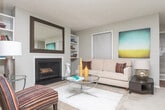 Located in Sandy Springs, Georgia, this single-floor residence offers a thoughtfully designed layout that balances comfort and functionality. The living room serves as the heart of the home, centered around a classic wood-burning fireplace flanked by built-in bookshelves and topped with a large decorative mirror. Multiple windows invite natural light into the space, and the room flows seamlessly into a dedicated dining area, making it well-suited for both relaxing and entertaining. The kitchen is outfitted with white cabinetry, dark granite-style countertops, stainless steel appliances including a gas range and over-the-range microwave, and warm hardwood-style flooring that adds a clean, modern finish. The spacious bedroom features soft wall-to-wall carpeting, a wall-mounted television, a walk-in closet with built-in shelving, and a secondary closet for additional storage. Natural light filters in through a window, creating a bright and restful atmosphere. The bathroom includes a shower with a curtain surround and hardwood-style flooring, maintaining the home's cohesive design language. Neutral tones, textured ceilings, and a practical single-floor plan make this residence in the 30350 zip code a comfortable and inviting home.