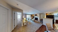 This well-designed single-floor residence at 700 Mallards Way in O'Fallon, Missouri offers a thoughtfully laid-out living space with a warm, neutral color palette throughout. The expansive living room serves as the heart of the home, anchored by a classic wood-burning fireplace and complemented by plush carpeting. Large sliding glass doors open to a private balcony, filling the space with natural light and providing outdoor views. The living area flows seamlessly into a dedicated dining space, which features rich hardwood flooring, an elegant pendant light fixture, and a pass-through window connecting to the kitchen. The kitchen is equipped with warm oak cabinetry, black appliances including an electric range and built-in microwave, and ample counter space. A utility area with an electrical panel is conveniently accessible from the kitchen. The bedroom offers a generous layout with carpet flooring, a bright window overlooking greenery, and ample room for furnishings. Two full bathrooms are finished with warm wood vanities, white countertops, and tub-shower combinations with hardwood-style flooring. The overall ambiance is inviting and practical, with consistent neutral tones and thoughtful details that make this residence a comfortable and functional home.