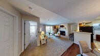 This well-designed single-floor residence at 700 Mallards Way in O'Fallon, Missouri offers a thoughtfully laid-out living space with a warm, neutral color palette throughout. The expansive living room serves as the heart of the home, anchored by a classic wood-burning fireplace and complemented by plush carpeting. Large sliding glass doors open to a private balcony, filling the space with natural light and providing outdoor views. The living area flows seamlessly into a dedicated dining space, which features rich hardwood flooring, an elegant pendant light fixture, and a pass-through window connecting to the kitchen. The kitchen is equipped with warm oak cabinetry, black appliances including an electric range and built-in microwave, and ample counter space. A utility area with an electrical panel is conveniently accessible from the kitchen. The bedroom offers a generous layout with carpet flooring, a bright window overlooking greenery, and ample room for furnishings. Two full bathrooms are finished with warm wood vanities, white countertops, and tub-shower combinations with hardwood-style flooring. The overall ambiance is inviting and practical, with consistent neutral tones and thoughtful details that make this residence a comfortable and functional home.