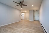 This single-floor unit offers a practical and comfortable layout across two bedrooms, a living room, a kitchen, and a closet. Light hardwood flooring runs throughout, creating a cohesive and clean aesthetic in every room.

The living room is a bright, open space featuring recessed lighting, a ceiling fan, and a large window with vertical blinds that allows natural light to fill the room while offering views of the surrounding greenery. Baseboard heating and a wall-mounted A/C unit provide year-round comfort.

The kitchen is well-equipped with white shaker-style cabinetry, granite countertops, and a full suite of white appliances including a refrigerator, electric range, dishwasher, and under-cabinet range hood. An adjacent open shelving closet provides convenient pantry storage.

The primary bedroom is a comfortable, well-lit space with a ceiling fan, a window with outdoor views, and a dedicated closet with a hanging rod. The second bedroom mirrors the same clean design with its own ceiling fan, natural light, and hardwood flooring.

Throughout the unit, neutral gray-toned walls, clean white trim, and consistent flooring create a bright, modern ambiance that is both inviting and functional.
