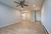 This single-floor unit offers a practical and comfortable layout across two bedrooms, a living room, a kitchen, and a closet. Light hardwood flooring runs throughout, creating a cohesive and clean aesthetic in every room.

The living room is a bright, open space featuring recessed lighting, a ceiling fan, and a large window with vertical blinds that allows natural light to fill the room while offering views of the surrounding greenery. Baseboard heating and a wall-mounted A/C unit provide year-round comfort.

The kitchen is well-equipped with white shaker-style cabinetry, granite countertops, and a full suite of white appliances including a refrigerator, electric range, dishwasher, and under-cabinet range hood. An adjacent open shelving closet provides convenient pantry storage.

The primary bedroom is a comfortable, well-lit space with a ceiling fan, a window with outdoor views, and a dedicated closet with a hanging rod. The second bedroom mirrors the same clean design with its own ceiling fan, natural light, and hardwood flooring.

Throughout the unit, neutral gray-toned walls, clean white trim, and consistent flooring create a bright, modern ambiance that is both inviting and functional.