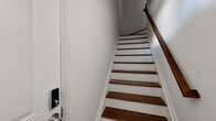 This two-floor space is thoughtfully designed with clean, modern finishes and a cohesive aesthetic carried throughout. Entry is made via a staircase featuring rich dark-stained wood treads contrasted against crisp white risers and trim, setting an inviting tone from the moment you arrive.

The kitchen is a standout feature, outfitted with two-tone cabinetry — dark lower cabinets paired with bright white upper cabinets — complemented by white quartz countertops and a classic subway tile backsplash. Stainless steel appliances, including a refrigerator, range, over-the-range microwave, and dishwasher, complete the well-appointed space. Deep dark hardwood flooring anchors the kitchen's contemporary feel.

The open living area flows naturally from the kitchen, bathed in a neutral palette and finished with wood-look flooring that adds warmth. Multiple bedrooms are spread across both floors, each featuring wood-look flooring, large windows that invite natural light, and clean white walls. One upper-floor bedroom includes a vaulted ceiling detail, adding architectural character, while another features a double closet for ample storage.

The bathroom is finished with wood-look tile flooring, white subway tile surrounding the tub-shower combination, and a decorative mosaic tile accent border, providing a clean and polished look throughout.