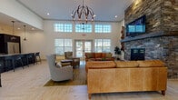 Located at 95 Salmon Brook Street in Granby, Connecticut, this single-floor community space is thoughtfully designed to offer a welcoming and functional environment. The centerpiece of the space is a spacious lounge area distinguished by soaring ceilings, clerestory windows that flood the room with natural light, and a dramatic floor-to-ceiling stacked stone fireplace with a wood mantle. Comfortable leather sofas and an ornate spherical chandelier complete the inviting atmosphere, while French doors provide views of the surrounding outdoor area.

Adjacent to the lounge is a well-appointed kitchen featuring dark espresso cabinetry, bold granite countertops with matching backsplash, stainless steel appliances, and a large island with bar seating illuminated by pendant lighting. A dedicated dining area with a substantial wood table and outdoor views serves as an ideal gathering space.

Additional seating nooks offer quieter retreats, furnished with upholstered armchairs and leather ottomans. Light-toned herringbone hardwood flooring flows consistently throughout, connecting each area seamlessly. Wide, well-lit corridors with elevator access and dual water fountains reflect attention to accessibility and practical detail throughout the space.