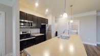 Located at 990 Plumway Ln in Lewis Center, Ohio, this single-floor residence offers a well-designed open-concept layout that seamlessly connects the kitchen, dining, and living areas. The kitchen is a standout feature, equipped with stainless steel appliances including a refrigerator, range, and microwave, all complemented by dark espresso cabinetry, light-toned countertops, and a large center island with a built-in sink. Pendant lighting above the island adds a polished touch, while recessed lighting throughout ensures a bright and welcoming atmosphere. The main living areas are finished with durable hardwood-style flooring, providing a clean, modern aesthetic. Bedrooms are carpeted for comfort and feature large windows with blinds that invite natural light and offer views of the surrounding greenery. The bathroom is neatly appointed with a tub-shower combination, a dark-framed vanity mirror, and wood-style flooring that ties in with the rest of the home. A dedicated in-unit laundry area houses a full-sized washer and dryer with additional overhead shelving for storage. Neutral wall tones throughout create a versatile backdrop suitable for a variety of interior styles.