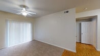 This single-floor residence offers a straightforward, functional layout designed for comfortable everyday living. The living area serves as the central gathering space, finished with neutral-toned carpet and equipped with a ceiling fan with integrated lighting. A full-width sliding glass door fitted with vertical blinds allows natural light to fill the room and provides access to the outdoors. The transition between the living area and the adjacent hallway reveals hardwood-style flooring that continues through the main corridor and into the kitchen.

The galley-style kitchen is efficiently organized, featuring warm wood-toned cabinetry on both sides, light countertops, a stainless steel sink, and white appliances including a refrigerator, stove, microwave, and dishwasher. A built-in desk nook tucked near the hallway offers a practical workspace. The bedroom is a comfortable, carpet-floored room with a ceiling fan, a window with blinds for natural light, and direct access to both a walk-in closet with shelving and a private bathroom. The bathroom includes a full tub and shower combo with white tile surround, wood-framed cabinetry, and a single vanity with sink.