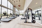 Located at 14020 Stream Way in Charlotte, NC, this state-of-the-art fitness center offers a spacious and thoughtfully designed exercise environment spanning a single open floor. The facility's most striking architectural feature is its dramatic double-height ceiling paired with expansive floor-to-ceiling windows that flood the interior with natural light and provide sweeping views of the surrounding neighborhood. Stylish pendant lighting and ceiling fans complement the bright, airy atmosphere throughout.

Light wood-tone flooring runs the length of the space, lending a clean and contemporary aesthetic. The main exercise area is comprehensively outfitted with a full row of treadmills and elliptical trainers positioned directly in front of the large windows, allowing users to enjoy the outdoor views during cardio sessions. Strength training is well-represented with a multi-station cable machine, free weight benches, and multiple racks of dumbbells.

A dedicated studio room, separated by frosted glass doors, houses spin bikes and a rowing machine alongside a large wall mirror and mounted flat-screen display — ideal for group fitness or individual cycling sessions. The overall ambiance is bright, modern, and energizing, making this fitness center a premium amenity for health-conscious users.