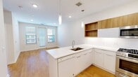Located at 101 Woodbine Road in Downingtown, PA, this one-bedroom, one-bathroom unit offers a thoughtfully designed layout with modern finishes throughout. The open-concept kitchen serves as the heart of the space, showcasing a large peninsula with a white quartz countertop and undermount sink, sleek white lower cabinetry, and warm wood-toned upper cabinets with open shelving. Stainless steel appliances — including a gas range, over-the-range microwave, and a French-door refrigerator — complete the well-appointed kitchen. Pendant lighting and recessed fixtures illuminate the space, while light hardwood flooring extends through the main living area. French doors allow natural light to flow in and provide access to an outdoor area. The bedroom offers a comfortable footprint with plush carpeting, neutral walls, and windows that bring in natural light. The bathroom continues the modern aesthetic with wood-grain cabinetry, a white quartz vanity top, light tile flooring, and a glass-enclosed walk-in shower with white subway tile surround. A dedicated laundry area houses a stacked Whirlpool washer and dryer, adding everyday convenience to this well-designed unit.