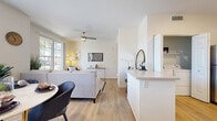 Located in Palm Desert, California, this well-appointed one-bedroom, one-bathroom residence offers a thoughtfully designed single-level layout that maximizes comfort and functionality. The open-concept living room is bright and welcoming, featuring wood-style flooring, a ceiling fan, and a sliding glass door that opens to a private patio, allowing natural light and outdoor views to flow seamlessly into the space. The kitchen is a standout feature, outfitted with crisp white cabinetry, a subtle tile backsplash, stainless steel appliances including a gas range, built-in microwave, dishwasher, and refrigerator, along with a breakfast bar that connects to the living area. A dedicated in-unit laundry closet with a full-size washer and dryer adds everyday convenience. The bedroom is a serene retreat with soft carpeting, vaulted ceiling accents, warm neutral tones, and a large window dressed with layered curtains that invite natural light. The bathroom features wood-style flooring, a white vanity with ample storage, a large mirror, and modern light fixtures. The hallway connects the spaces cohesively, completing this efficient and stylish Palm Desert home.