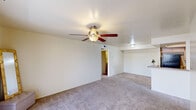 Located in Glendale, Arizona, this single-floor residence offers two bedrooms and two bathrooms with a functional, well-organized layout. The combined kitchen and living area forms the heart of the home, where the living room features neutral carpet, a ceiling fan with light fixture, and sliding glass doors that invite natural light and outdoor views. The kitchen is equipped with black appliances — including a refrigerator and range — light wood cabinetry, a double sink, and a distinctive tray ceiling with recessed lighting that adds architectural character to the space. Both bedrooms are carpeted and include ceiling fans. The primary bedroom is generously sized, with a large window for natural light and access to a walk-in closet featuring multiple hanging rods and shelving. The second bedroom also benefits from a window and ceiling fan. Both bathrooms are finished with warm wood-look flooring and light cabinetry. One bathroom includes a shower-tub combination with a curtain rod and a wide vanity with ample under-sink storage. The second bathroom mirrors this aesthetic with a similarly appointed vanity and mirror. A dedicated hallway and entrance area complete the layout, offering a clean, cohesive flow throughout the residence.