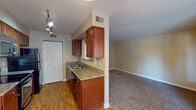 This single-floor residence offers a practical and cohesive layout designed for comfortable everyday living. The kitchen serves as a functional centerpiece, featuring rich cherry-toned cabinetry, granite countertops, a stainless steel sink, and a full suite of black appliances including an electric range, over-the-range microwave, and refrigerator. Track lighting illuminates the space, while wood-look flooring adds warmth underfoot. The kitchen flows seamlessly into the adjacent living area, which is finished with plush carpeting and neutral-toned walls, creating a cozy and inviting atmosphere. A dedicated dining area sits just beyond, distinguished by light hardwood-style flooring, a chandelier overhead, and large windows alongside a sliding glass door that floods the space with natural light and provides access to the outdoors. The bedroom is a quiet, carpeted retreat with a window that brings in additional natural light. The full bathroom is cleanly finished with a tub-shower combination, white tile surround, granite-topped vanity with cherry cabinetry, and matching wood-look flooring. A spacious closet with bifold doors adds practical storage. Throughout the space, consistent finishes and a warm neutral palette create a unified and inviting environment.