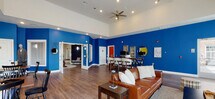 Located at 310 NJ-31 in Flemington, New Jersey, this single-floor community clubhouse is a lively, well-appointed gathering space designed for socializing and recreation. The interior makes a bold visual statement with striking cobalt blue and chartreuse yellow accent walls contrasted against crisp white trim and warm hardwood-style flooring that flows throughout the entire space.

The main lounge area serves as the heart of the clubhouse, featuring soaring vaulted ceilings, a ceiling fan, and a sleek linear gas fireplace flanked by a wall-mounted television. Comfortable leather seating and generous natural light from multiple white-framed windows create a welcoming atmosphere. French doors lead to an outdoor area, further enhancing the sense of openness.

Adjacent to the lounge is a dedicated billiards room, providing a casual recreational space for residents. A cozy TV lounge with soft seating and a wall-mounted screen offers a quieter retreat. The dining nook, dressed in vibrant yellow-green, features bistro-style tables and chairs alongside curated artwork, adding a cheerful character to the space.

The full kitchen is outfitted with dark espresso cabinetry, a white subway tile backsplash, light countertops, stainless steel appliances, and a large breakfast bar with seating illuminated by elegant pendant lighting. A workstation area rounds out this multifunctional clubhouse, making it a comprehensive hub for community life.