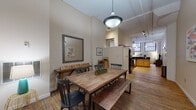 Located at 1278 W Ninth St in Cleveland's dynamic Ohio City neighborhood, this single-floor loft-style unit at The Bingham blends industrial character with modern comfort. The open-concept living and dining area is anchored by richly patinated hardwood floors, soaring ceilings, and dramatic painted brick walls that rise to tall, grid-paned windows, flooding the space with natural light. Industrial-style pendant lighting adds to the loft aesthetic throughout. The dining area offers generous room for a full-sized table and bench seating, flowing seamlessly into a well-equipped kitchen outfitted with warm maple cabinetry, dark granite countertops, a tile backsplash, and black appliances including a range, microwave, and refrigerator. The living area is a relaxed retreat defined by exposed brick, hardwood floors, and large windows. The space includes two bedrooms, each carpeted for comfort, with ample ceiling height and natural light. One bedroom features exposed ductwork, a hallmark of the building's converted industrial heritage. Two bathrooms serve the unit, each featuring granite-topped vanities, warm wood cabinetry, and tile flooring. Together, these elements create a thoughtfully designed urban living space that honors its architectural roots.