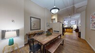 Located at 1278 W Ninth St in Cleveland's dynamic Ohio City neighborhood, this single-floor loft-style unit at The Bingham blends industrial character with modern comfort. The open-concept living and dining area is anchored by richly patinated hardwood floors, soaring ceilings, and dramatic painted brick walls that rise to tall, grid-paned windows, flooding the space with natural light. Industrial-style pendant lighting adds to the loft aesthetic throughout. The dining area offers generous room for a full-sized table and bench seating, flowing seamlessly into a well-equipped kitchen outfitted with warm maple cabinetry, dark granite countertops, a tile backsplash, and black appliances including a range, microwave, and refrigerator. The living area is a relaxed retreat defined by exposed brick, hardwood floors, and large windows. The space includes two bedrooms, each carpeted for comfort, with ample ceiling height and natural light. One bedroom features exposed ductwork, a hallmark of the building's converted industrial heritage. Two bathrooms serve the unit, each featuring granite-topped vanities, warm wood cabinetry, and tile flooring. Together, these elements create a thoughtfully designed urban living space that honors its architectural roots.
