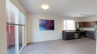 Located at 1202 S Shelby St in Indianapolis, Indiana, this single-floor unit sits within the vibrant Fountain Square neighborhood. The interior presents an open-concept layout that seamlessly connects the living area with a kitchenette or wet bar setup. The living space features neutral-toned carpeting and clean white walls, creating a bright and versatile canvas suited for a variety of uses.

A sliding glass door along one wall floods the space with natural light and offers convenient access to the exterior, while horizontal blinds provide privacy control. A second window positioned above the sink area reinforces the sense of openness and brings in additional daylight.

The kitchen or kitchenette component includes dark-stained lower cabinetry paired with a double-basin sink, offering functional utility within a compact footprint. Flush ceiling lighting provides consistent illumination throughout the space. The overall design is clean and modern, with simple finishes and a neutral palette that allow the space to adapt to its intended purpose. The open floor plan and natural light make this a practical and welcoming single-level space.