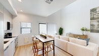Located in Phoenix, AZ, this two-story, 2-bedroom, 2-bathroom home offers a thoughtfully designed layout across two floors. The main level features an open-concept kitchen and living area with soaring vaulted ceilings that amplify the sense of space and light. The kitchen is outfitted with stainless steel appliances, flat-front cabinetry extending to the ceiling, a white tile backsplash, and a clean white countertop — a sleek, functional design. The living and dining area flows seamlessly, with light hardwood flooring, a sliding glass door opening to an outdoor space, and large windows inviting abundant natural light. Upstairs, a bright hallway with recessed lighting connects the two bedrooms and bathrooms. The primary bedroom features plush carpeting, generous windows with drape panels, and ample room to furnish comfortably. The second bedroom includes a ceiling fan, an accent wall in a muted teal tone, and natural light. Both bathrooms are finished in a modern style, with one showcasing a glass-enclosed walk-in shower, black hardware accents, and a white vanity. The overall aesthetic is clean, contemporary, and bright, creating a cohesive and welcoming atmosphere throughout.
