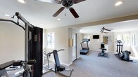 The fitness center at 3634 College in Oceanside is a well-appointed single-floor facility designed to support a variety of workout routines. The space is organized into distinct exercise zones, allowing users to move comfortably between cardio and strength training areas without congestion.

The interior features neutral beige walls, crown molding, and wall-to-wall carpet, contributing to a clean and comfortable environment. Two ceiling fans are positioned throughout the space, promoting consistent air circulation during workouts.

The cardio zone is equipped with a treadmill and an additional cardio machine, both positioned on protective floor mats. A wall-mounted flat-screen television is installed nearby, offering entertainment during exercise sessions. Large mirrors line portions of the walls, enhancing the sense of openness and allowing users to monitor their form.

The strength training area includes a multi-function cable machine and a weight bench, providing options for resistance-based workouts. Natural light enters through windows along the exterior wall, keeping the space bright and inviting. A French door provides access to the exterior, adding to the overall functionality and ventilation of the facility.