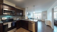 Located at 1386 E 105th St in Cleveland, Ohio, this well-appointed single-floor residence offers a thoughtfully designed open-concept layout. The kitchen is a standout feature, showcasing rich dark espresso cabinetry, granite countertops, a tile backsplash, and a full suite of stainless steel appliances including a range, over-the-range microwave, and dishwasher. A peninsula with pendant lighting above serves as both a functional workspace and a natural transition into the living and dining areas. The living room is bright and welcoming, benefiting from a large window that invites natural light and offers views of the surrounding neighborhood. Dark hardwood-style flooring runs throughout the main living spaces, adding warmth and continuity to the design. A dedicated dining area adjacent to the living room provides a comfortable spot for meals. The bedroom is a serene retreat with neutral walls, a window for natural light, and access to a walk-in closet. The bathroom features matching dark wood cabinetry with granite countertops, a large vanity mirror, and a shower-tub combination. Clean lines, neutral tones, and modern finishes give this residence a cohesive and contemporary feel throughout.