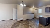 This single-floor residence offers a well-designed open-concept layout that seamlessly connects the kitchen, dining, and living areas. The kitchen is a standout feature, equipped with rich dark espresso cabinetry, generous counter space with light-toned laminate countertops, a double-basin sink, and a full suite of black appliances including a refrigerator, range, and over-the-range microwave. A large peninsula provides additional prep space and serves as a natural divider between the kitchen and the adjacent living and dining areas.

The living and dining spaces benefit from vaulted ceilings that enhance the sense of openness, complemented by an elegant chandelier that adds a refined touch. Wood-look plank flooring runs throughout the main living areas, transitioning to plush carpeting in the bedrooms. The bedrooms are bright and airy, each featuring windows with blinds that allow for natural light and privacy.

The bathroom is clean and functional, featuring a full tub-shower combination with white surround, wood-look tile flooring, and neutral wall tones that maintain a cohesive aesthetic throughout. Dark wood trim and door frames provide consistent contrast against the warm beige walls, tying the design elements of the space together cohesively.
