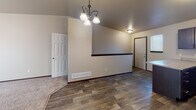 This single-floor residence offers a well-designed open-concept layout that seamlessly connects the kitchen, dining, and living areas. The kitchen is a standout feature, equipped with rich dark espresso cabinetry, generous counter space with light-toned laminate countertops, a double-basin sink, and a full suite of black appliances including a refrigerator, range, and over-the-range microwave. A large peninsula provides additional prep space and serves as a natural divider between the kitchen and the adjacent living and dining areas.

The living and dining spaces benefit from vaulted ceilings that enhance the sense of openness, complemented by an elegant chandelier that adds a refined touch. Wood-look plank flooring runs throughout the main living areas, transitioning to plush carpeting in the bedrooms. The bedrooms are bright and airy, each featuring windows with blinds that allow for natural light and privacy.

The bathroom is clean and functional, featuring a full tub-shower combination with white surround, wood-look tile flooring, and neutral wall tones that maintain a cohesive aesthetic throughout. Dark wood trim and door frames provide consistent contrast against the warm beige walls, tying the design elements of the space together cohesively.