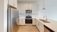 Located at 1001 Boopa Ln in Mount Pleasant, South Carolina, this single-floor residence offers a thoughtfully designed layout with a clean, contemporary aesthetic. The open-concept living and dining area is anchored by light wood-look flooring, white walls, and a ceiling fan, creating a bright and airy atmosphere. Large windows invite abundant natural light while offering views of the surrounding area.

The kitchen is a standout feature, equipped with stainless steel appliances including a refrigerator, electric range, and over-the-range microwave. Light-toned shaker-style cabinetry reaches toward the ceiling, complemented by a subway tile backsplash and a spacious peninsula with a quartz-style countertop and an undermount sink. Stylish teal pendant lights add a modern, distinctive touch above the peninsula.

The bedroom is generously sized with plush carpeting, dual windows fitted with blinds, and a ceiling fan, providing a comfortable and well-lit retreat. A peek at the exterior through the bedroom windows hints at a balcony access point nearby.

The bathroom features wood-look flooring, a white vanity with quartz countertop, a large mirror, a soaking tub with shower combination, and clean, bright finishes throughout. The overall design of this residence balances functionality with modern style in a welcoming Mount Pleasant setting.