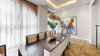 Located in Miramar, FL, this refined interior space showcases a seamless blend of contemporary design and artistic flair. The single-floor layout comprises two distinct areas, making efficient use of the available footprint without sacrificing elegance or functionality.

The standout feature is the formal dining area, anchored by a substantial dark wood table surrounded by sleek, high-backed chairs upholstered in cream with bold black trim. Overhead, a striking gold rod chandelier hangs from a coffered ceiling fitted with recessed lighting and integrated cove illumination, casting a warm, inviting glow throughout the space.

The flooring is a defining element — a geometric parquet wood pattern in a herringbone-inspired layout adds depth and visual interest underfoot. Floor-to-ceiling sheer curtains allow natural light to filter softly into the room, creating an airy ambiance. A lush fiddle-leaf fig plant introduces a touch of organic warmth to the otherwise polished environment.

Vibrant, large-scale abstract paintings serve as bold focal points on the walls, infusing the space with energy and color. A built-in open shelving unit with glass partitions displays colorful decorative vases, adding an artful, gallery-like quality. The overall atmosphere is one of curated luxury — modern, bright, and thoughtfully composed.