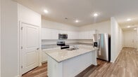 Located at 4236 Hollow Wind Way in Summerville, SC, this single-story home presents a clean, modern interior designed for comfortable everyday living. The open-concept layout connects the kitchen and living areas seamlessly, with wood-look luxury vinyl plank flooring extending throughout the main living spaces and recessed lighting illuminating the interiors.

The kitchen is a standout feature, equipped with white shaker-style cabinetry, granite countertops, and a full suite of stainless steel appliances including a refrigerator with ice maker, electric range, and built-in microwave. A central island with an integrated sink provides additional workspace and casual seating, while windows overlooking the living area allow natural light to flow freely throughout.

The bedrooms are carpeted for comfort, with windows admitting natural light and generous closet space, including a walk-in closet outfitted with wire shelving systems. The primary bathroom offers a double vanity with white cabinetry, a framed walk-in shower with glass doors, and wood-look flooring. A secondary bathroom features a single vanity with a mirror and classic fixtures. A dedicated laundry area with wire shelving and utility hookups rounds out this well-organized home.