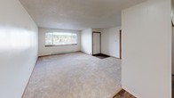 Located on Ashcrest Loop NE in Poulsbo, Washington, this single-floor unit offers a practical and comfortable layout designed for everyday living. The open living and dining area is generously sized, featuring soft neutral carpet, a textured ceiling, and a large picture window that frames outdoor views and fills the space with natural light. Baseboard heating runs along the exterior walls, providing consistent warmth throughout.

The galley-style kitchen is efficiently arranged with warm wood-toned cabinetry lining both sides, light countertops offering ample prep space, a stainless steel sink, and white appliances including an electric range and refrigerator. A window above the countertop brings in additional natural light.

Two carpeted bedrooms provide comfortable retreats, each with neutral tones, textured ceilings, and closet storage. The bedrooms share a full bathroom finished with wood-look vinyl flooring, warm oak cabinetry with a single vanity sink, a toilet, and a full tub and shower combination with white tile surround. A mirrored medicine cabinet completes the bathroom.

Throughout the unit, warm wood-look flooring in the kitchen and bathroom contrasts with the plush carpet in the living and sleeping areas, creating a cohesive and functional living environment.