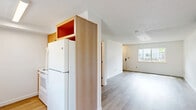 This two-bedroom, two-bathroom two-story unit offers a practical and well-organized layout across two floors. The main level features a light-filled living area with light wood-style plank flooring, crisp white walls, and a wall-mounted mini-split air conditioning unit for climate control. The adjacent kitchen is equipped with wood-toned cabinetry, open upper shelving, and white appliances, opening toward the living space for a connected feel. A carpeted staircase with a metal handrail leads to the upper level, where both bedrooms are located. Each bedroom features the same light wood-style flooring, a ceiling fan with integrated lighting, and windows that bring in natural light and exterior views. The primary bedroom includes an open closet with wire shelving and convenient access to a full bathroom. The full bathroom on the upper level features a tub-shower combination, a single-sink vanity with wood cabinetry and white countertop, and clean tile flooring. A second, more compact bathroom on the lower level includes a single-sink vanity and toilet, serving as a convenient half-bath alternative. Throughout the unit, textured ceilings, neutral tones, and consistent finishes create a cohesive, move-in ready atmosphere.
