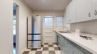 This single-floor home presents a thoughtfully arranged layout with a blend of classic and retro design elements throughout. The living areas are defined by rich, dark hardwood floors that run continuously, reflecting natural light and lending warmth to the open, neutral-toned spaces. Exposed beam detailing accents the ceiling in the main living area, adding architectural character, while large windows fitted with roller shades allow for generous natural light and outdoor views.

The kitchen carries a distinctly retro aesthetic, featuring powder-blue metal cabinetry paired with white countertops and a classic checkerboard vinyl floor in grey and cream tones. A stainless steel refrigerator and a gas range complete the functional cooking space, while a door with a windowed panel provides direct exterior access and brings additional natural light into the room.

The bathroom is a standout feature, showcasing floor-to-ceiling turquoise ceramic tile surrounding a full bathtub, complemented by a small window above — a bold, vintage-inspired design choice that gives the room a distinctive personality.

Additional rooms include well-proportioned bedrooms with hardwood flooring and large windows offering outdoor views, along with built-in shelving visible in the doll's-eye floorplan view, providing practical storage solutions throughout the home.