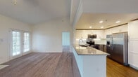 This single-story residence showcases an open, airy design anchored by a generously sized living room with soaring vaulted ceilings and plush carpeting throughout. A marble-surround fireplace serves as a focal point in the living area, complemented by French doors that invite natural light and provide views of surrounding greenery. A sliding glass door in an adjoining room offers additional outdoor access and further enhances the connection to the exterior.

The kitchen is well-appointed with two-tone cabinetry—white upper cabinets paired with grey lower cabinets—set against a subtle tile backsplash. Granite countertops extend to a peninsula that opens toward the living space, and stainless steel appliances including a refrigerator, range, and over-the-range microwave complete the functional layout. Wood-look flooring grounds the kitchen area.

The bedrooms feature soft carpeting and ceiling fans, with one room including a walk-in closet. Both bathrooms offer tub-shower combinations with white tile surrounds, chrome fixtures, and wood-look flooring. The overall palette is neutral and clean, creating a bright, move-in-ready atmosphere throughout.