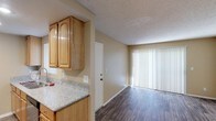This single-floor residence offers a practical and comfortable layout designed for everyday living. The open-concept living area is anchored by durable wood-style flooring and features a large sliding glass door dressed with vertical blinds, allowing generous natural light to fill the space. The kitchen is efficiently designed with warm honey-toned wood cabinetry, granite-look countertops, recessed lighting, and a full suite of stainless steel appliances including an electric range, microwave, and refrigerator. A peninsula-style counter provides additional workspace and a natural transition between the kitchen and the main living area. The bedrooms are carpeted in neutral tones, offering a soft and quiet retreat, and are brightened by windows with vertical blinds. One bedroom includes a spacious walk-in closet outfitted with double hanging rods and built-in shelving, providing ample storage. The bathroom features a clean, all-white tub and surround. Throughout the residence, warm beige walls, textured ceilings, and white baseboards create a cohesive and inviting aesthetic. The floor plan flows logically from the entry through the living and dining areas to the private sleeping quarters, making the most of the available space.