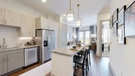 Located in Frisco, TX, this well-appointed one-bedroom, one-bathroom residence offers a cohesive and modern design throughout its efficiently utilized single floor. The open-concept kitchen and living area serves as the heart of the home, where the kitchen impresses with granite countertops, gray shaker-style lower cabinets, light wood upper cabinetry, a subway tile backsplash, and a full suite of stainless steel appliances including a range, microwave, dishwasher, and refrigerator. Wood-look flooring flows throughout the main living areas, anchoring the bright and airy atmosphere. The living room is generously proportioned, featuring large double French doors that open to an outdoor balcony, allowing abundant natural light and views of the surrounding landscape. The bedroom offers plush carpeting, multiple windows with outdoor views, and a calm, neutral palette. Adjacent to the bedroom is a well-organized walk-in closet with built-in shelving and dual hanging rods. The bathroom is finished with a granite-topped vanity, gray cabinetry, wood-look flooring, and a full tub-shower combination. Clean white walls and consistent, contemporary finishes create a polished and cohesive ambiance throughout the entire space.