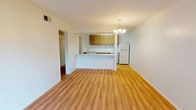 This single-floor unit offers three bedrooms and one and a half bathrooms within a practical, well-organized layout. The open-concept living and dining area is anchored by wood-look laminate flooring and illuminated by a chandelier overhead. A peninsula-style kitchen divides the space, featuring warm wood cabinetry, white appliances including an electric range and refrigerator, a stainless steel sink, and light countertops that extend along both sides for ample workspace.

Each of the three bedrooms is carpeted and includes a window that brings in natural light, along with a built-in closet with shelving for organized storage. One bedroom features a sliding glass door with vertical blinds that opens to a fenced outdoor area, providing a private exterior connection. The bedrooms offer a quiet, neutral atmosphere suitable for a variety of uses.

The half bathroom is clean and straightforward, finished with tile flooring. The overall color palette throughout the unit is neutral, with white walls and light finishes that create a bright, cohesive feel. The floor plan provides a functional flow between the living, kitchen, and bedroom areas.